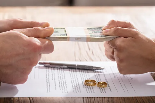 Two people holding money tensely over divorce documents and wedding rings