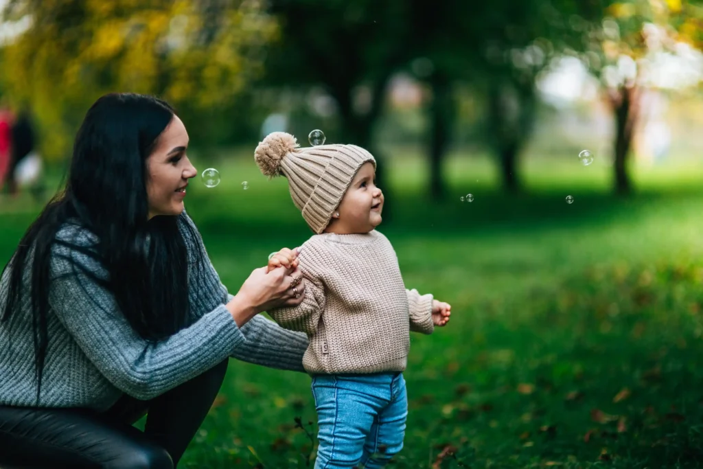 A mother holding up her baby looking at a bubble outside.