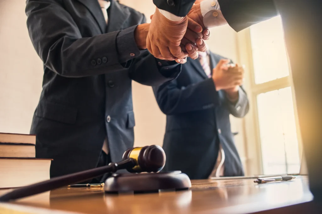 Close-up of legal professionals shaking hands next to a gavel and law books during a successful adoption case in a New Braunfels courtroom.